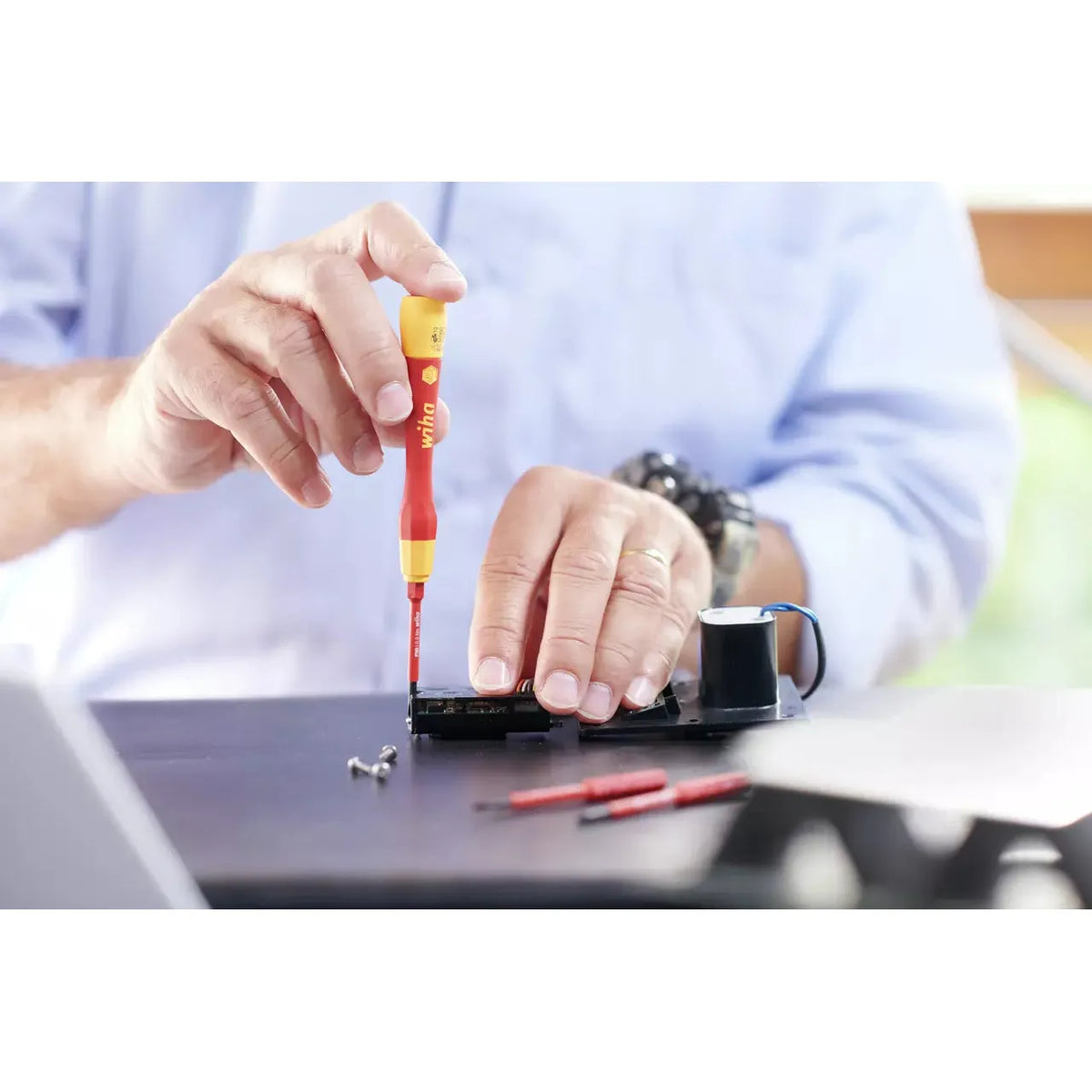 Person using a red and yellow precision screwdriver on electronic device