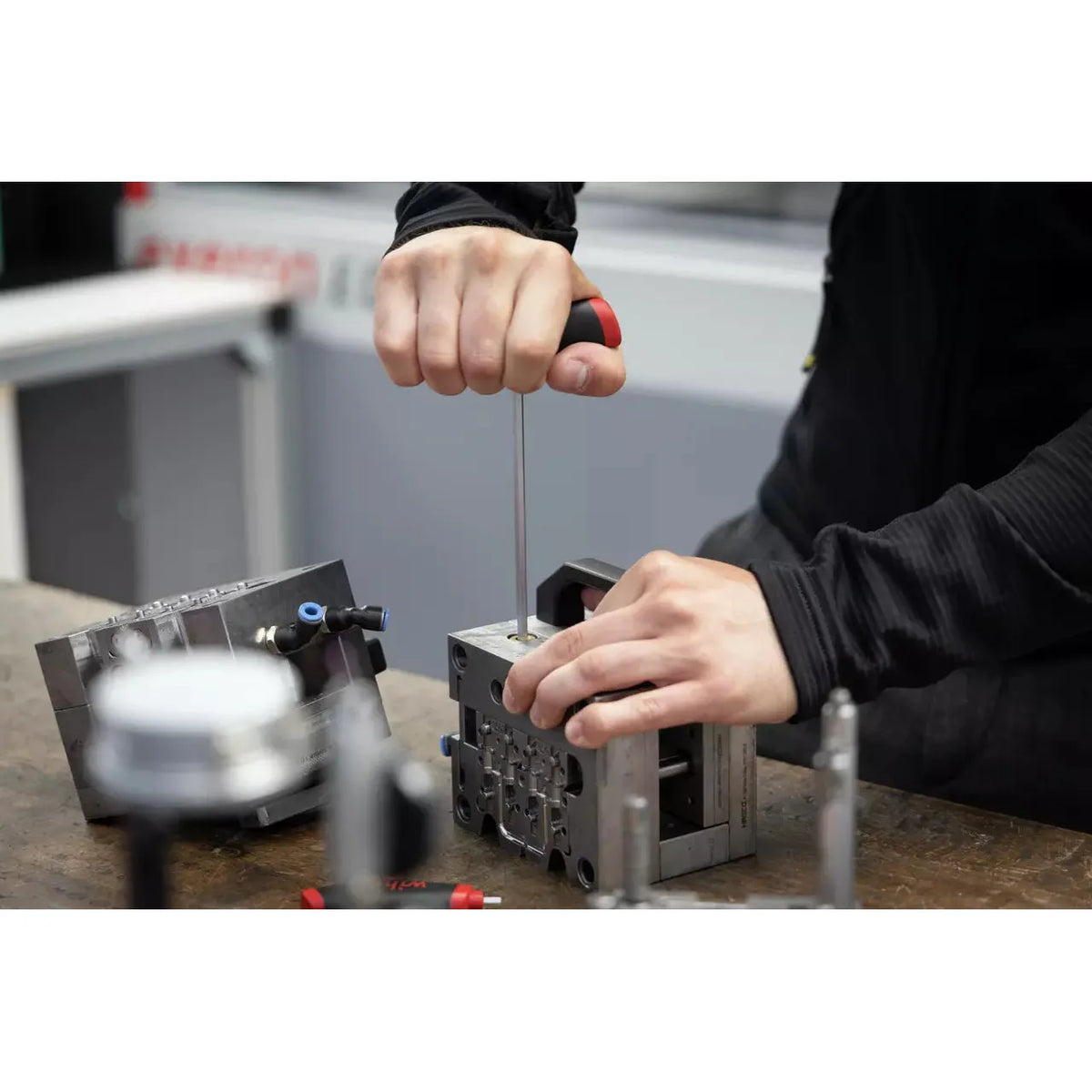 Person using a screwdriver to work on a metal block on a workbench.