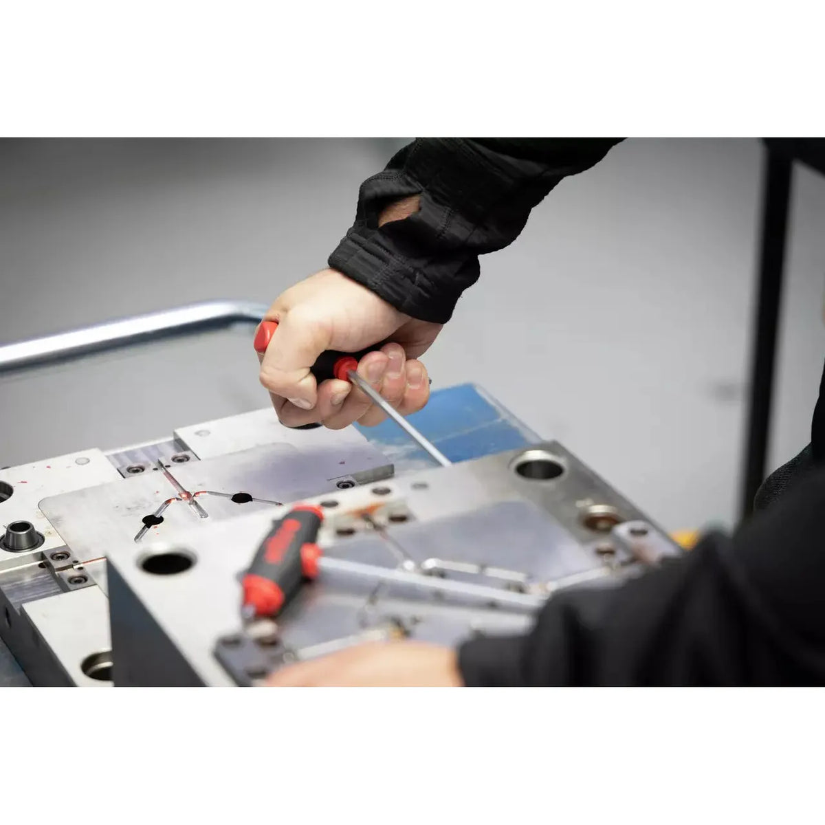 A person using a screwdriver on a metal surface, with another tool nearby.