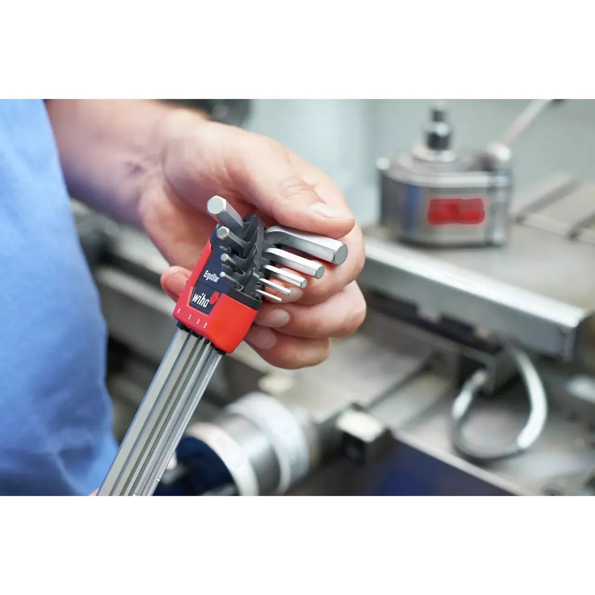 A person holds a set of hex keys in a red holder, with machinery in the background.