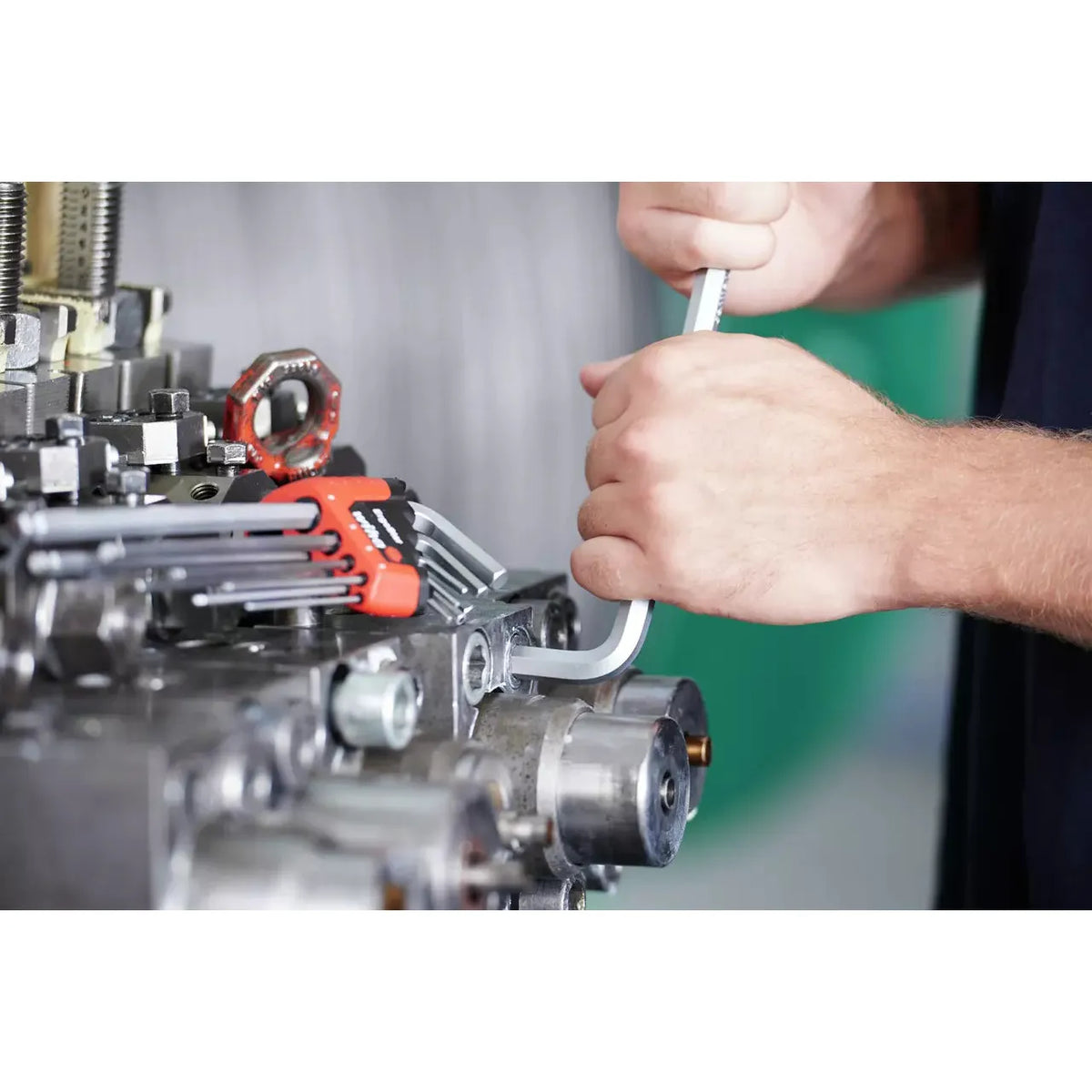 Person using a hex key on machinery with a set of hex keys nearby.