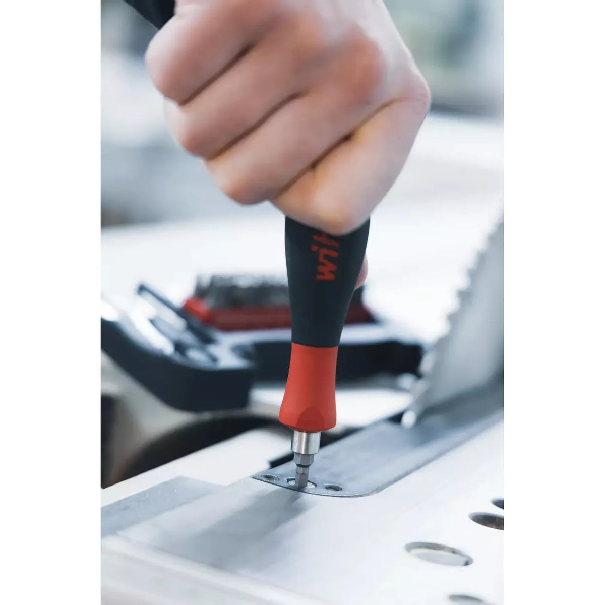 Person using a screwdriver to fasten a screw on a metal surface.