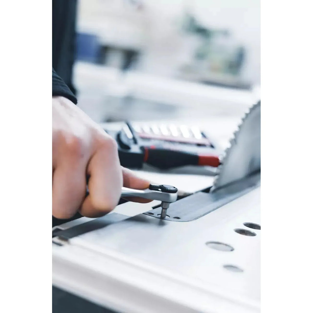 Person using a ratchet wrench to tighten a bolt on a metal surface near a circular saw blade.