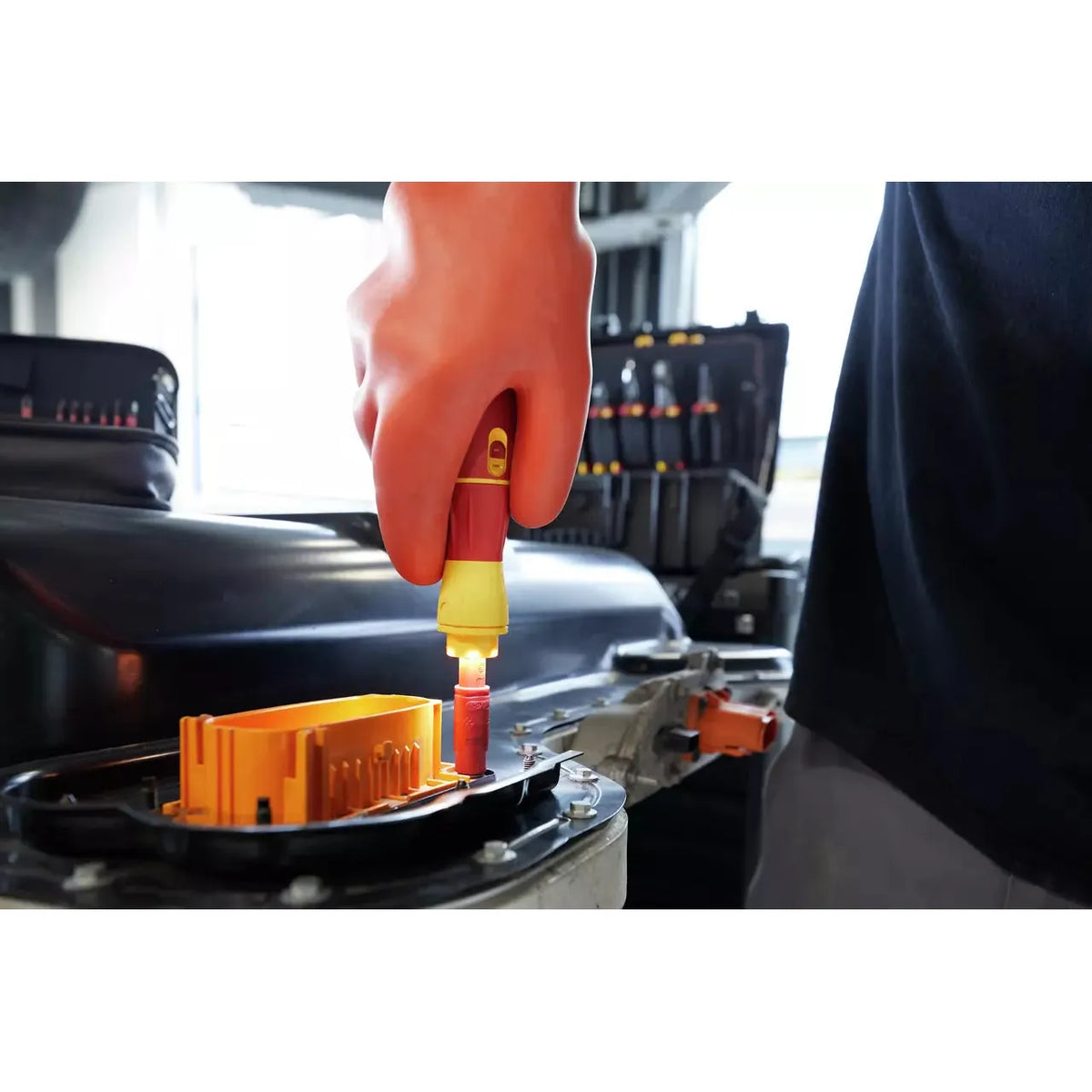 Person using an electric screwdriver on a car battery with orange gloves