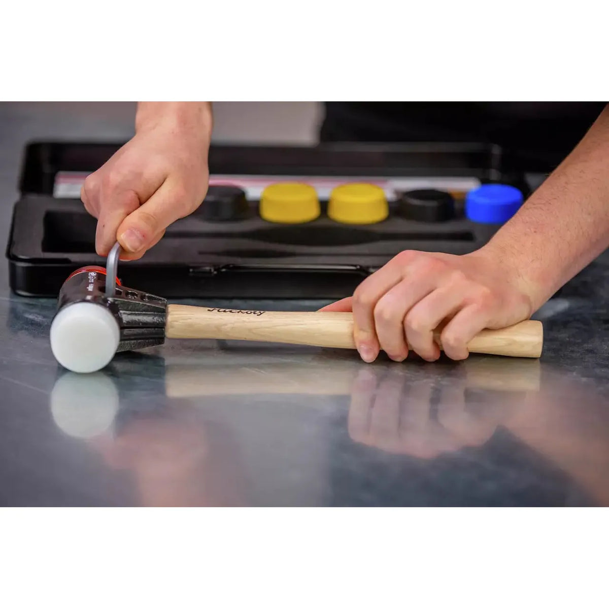 Person holding a mallet with a wooden handle, alongside interchangeable rubber caps in a case.