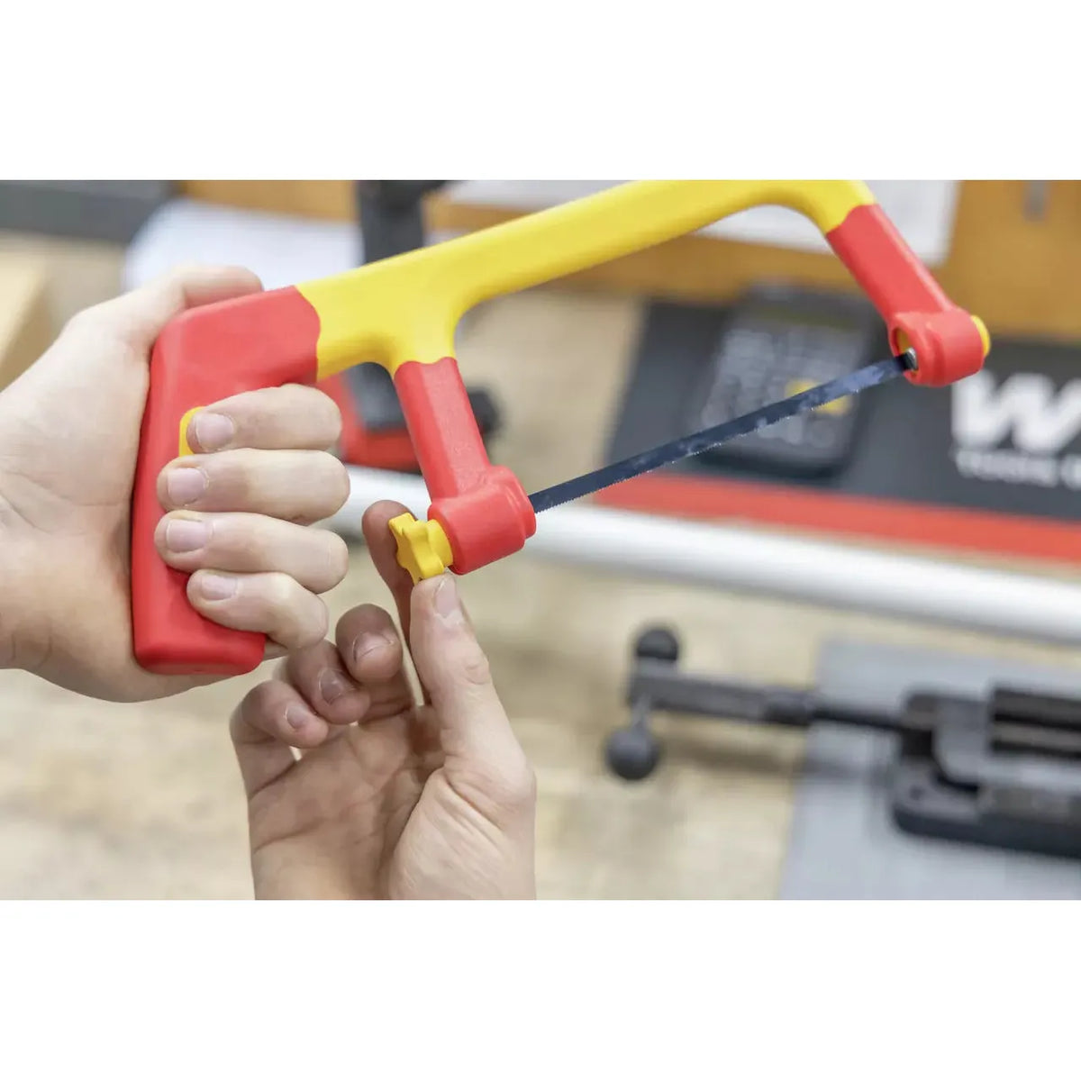A person adjusts a red and yellow hacksaw with a small knob