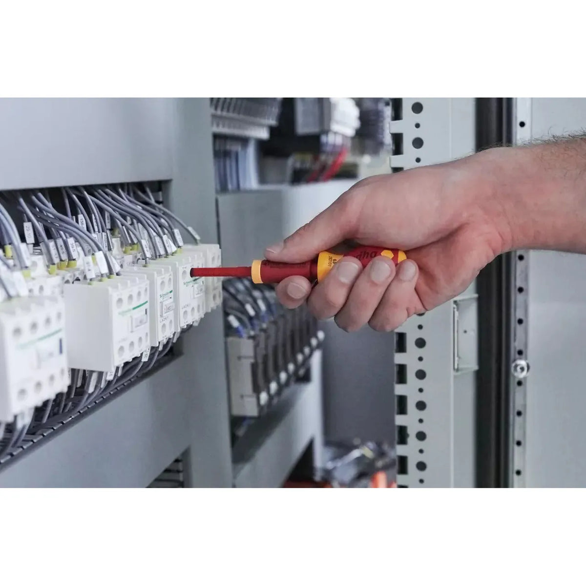 A person using an insulated screwdriver on an electrical panel.