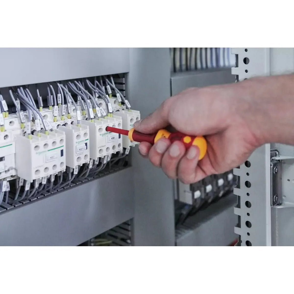 Person using an electric screwdriver on a control panel with wires.