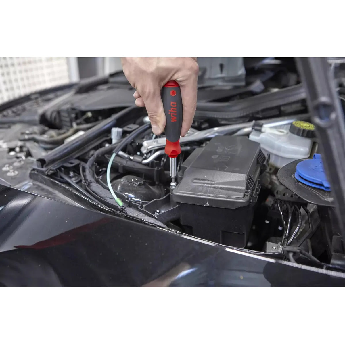 Person using a screwdriver on a car engine part.