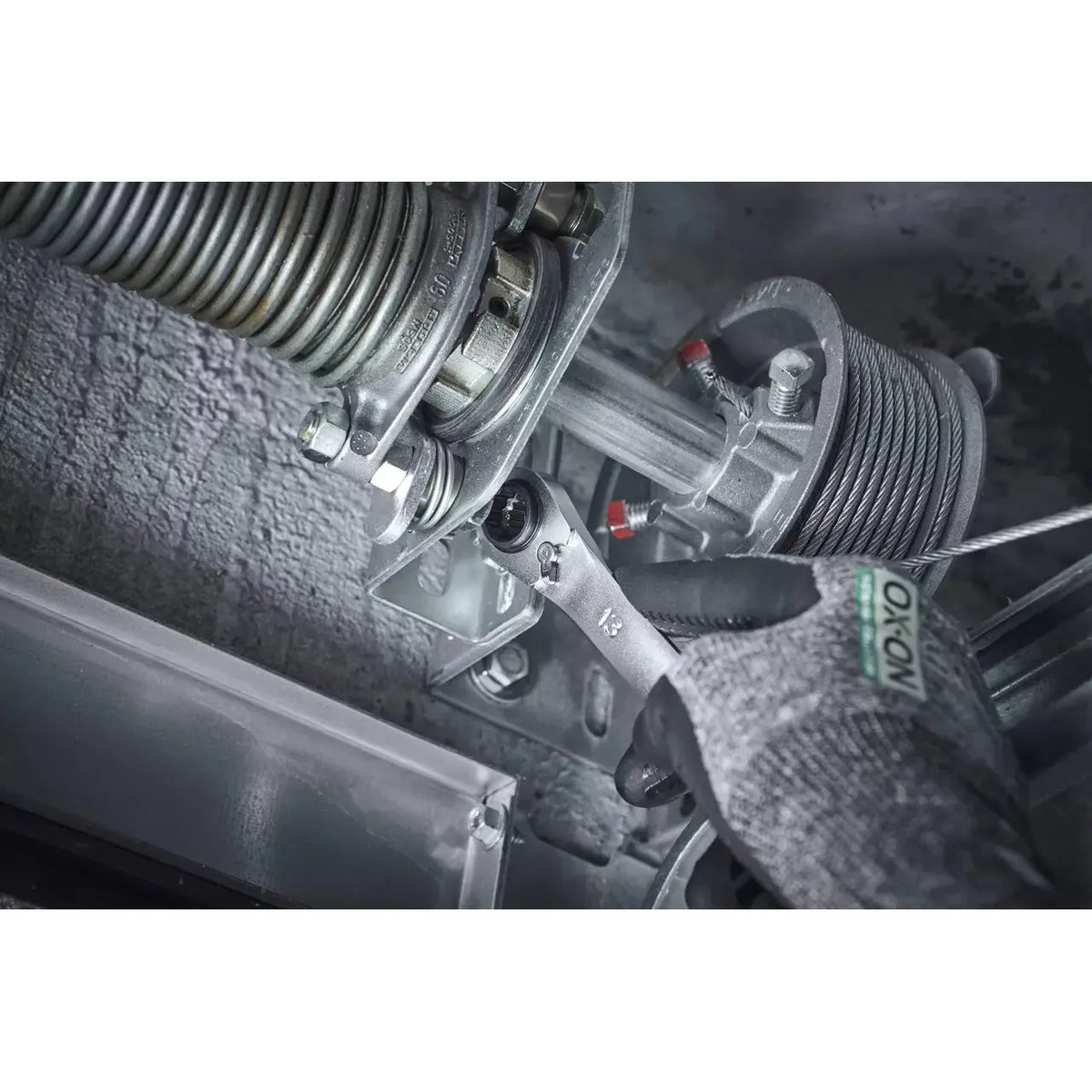 A hand in a glove uses a ratchet wrench on a metal garage door mechanism.