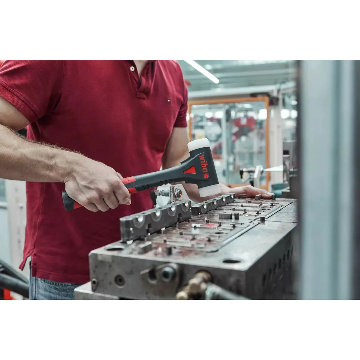 A person using a dead-blow hammer on a metal surface in an industrial setting.