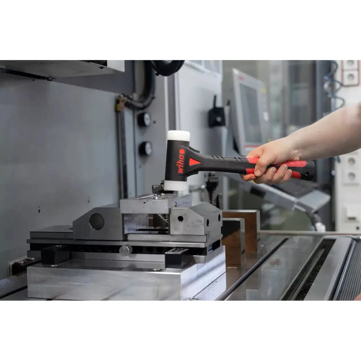 A person using a black and red dead-blow hammer on a metal vise in a workshop.