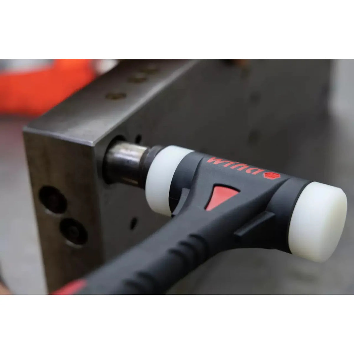 A black rubber mallet with white ends striking a metal surface