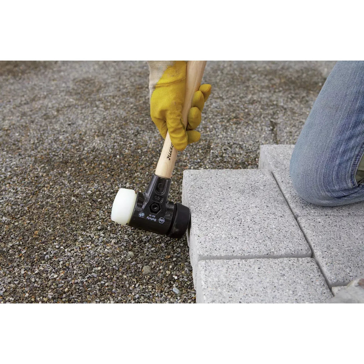 A person using a rubber mallet to adjust paving stones on gravel ground.