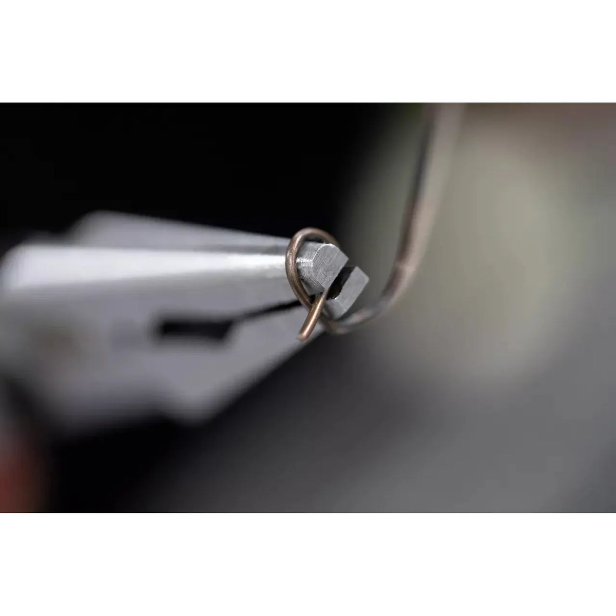 Close-up of pliers holding a bent metal wire loop