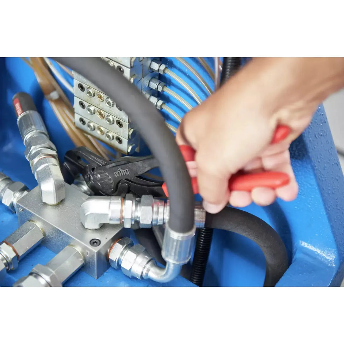 A person using a red-handled tool on metal pipes in a hydraulic system.