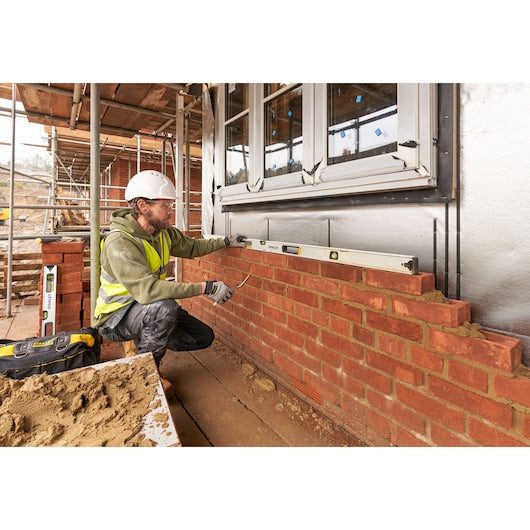 STANLEY FMHT43678-1 spirit level used by a worker checking horizontal alignment on a brick wall, side view.