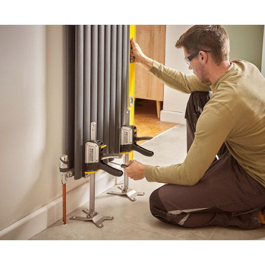 Photo of STANLEY FMHT83550-1 clamps securing a radiator during installation, used by a person kneeling indoors.