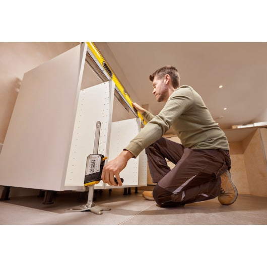 Photo of person using STANLEY FMHT83550-1 cabinet jack tool to level kitchen cabinets during installation.
