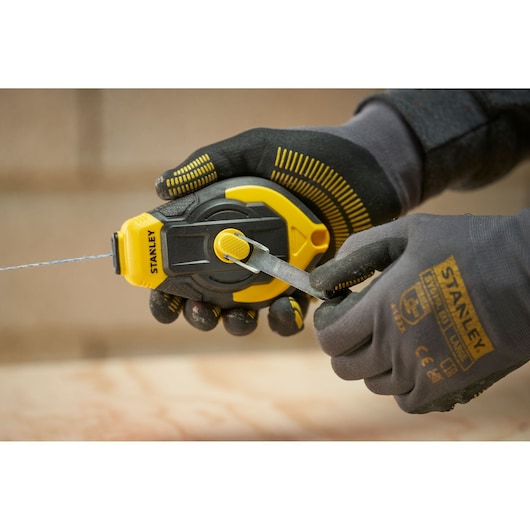 STANLEY STHT47311-0 chalk reel held in gloved hands, yellow and black design, product in use.