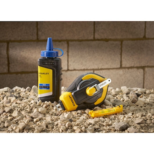 Stanley STHT47312-0 chalk line set with yellow chalk reel and blue chalk bottle on rocky surface.