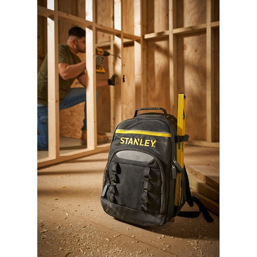 STANLEY STST1-72335 black tool backpack with yellow accents and level, on construction site floor.