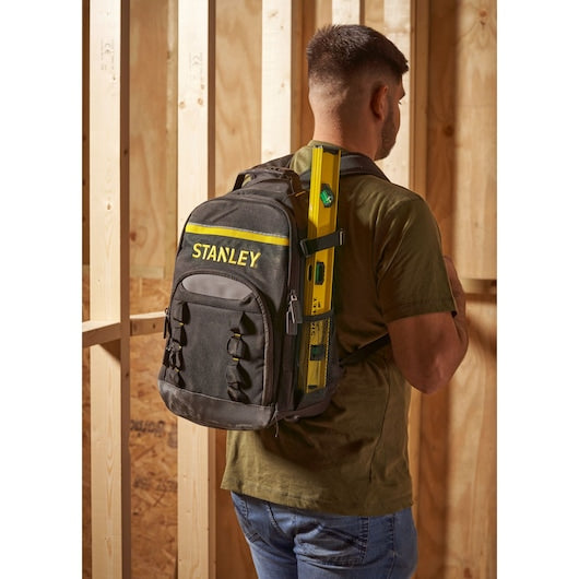 Stanley STST1-72335 black and yellow backpack worn by a man in a workshop, holding a level tool.