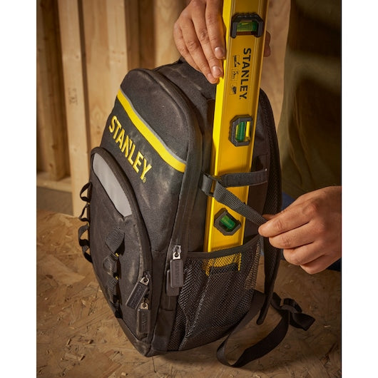 STANLEY STST1-72335 photography of black backpack with yellow logo, side mesh pocket holding level tool.