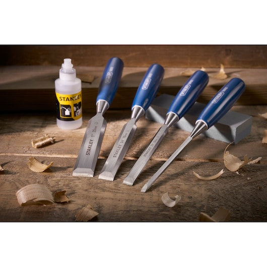 Photo of STANLEY 0-16-130 woodworking chisel set with blue handles and bottle on a wooden workbench.