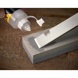 STANLEY 0-16-130 oil being applied to a sharpening stone with a chisel on wooden surface, close-up.