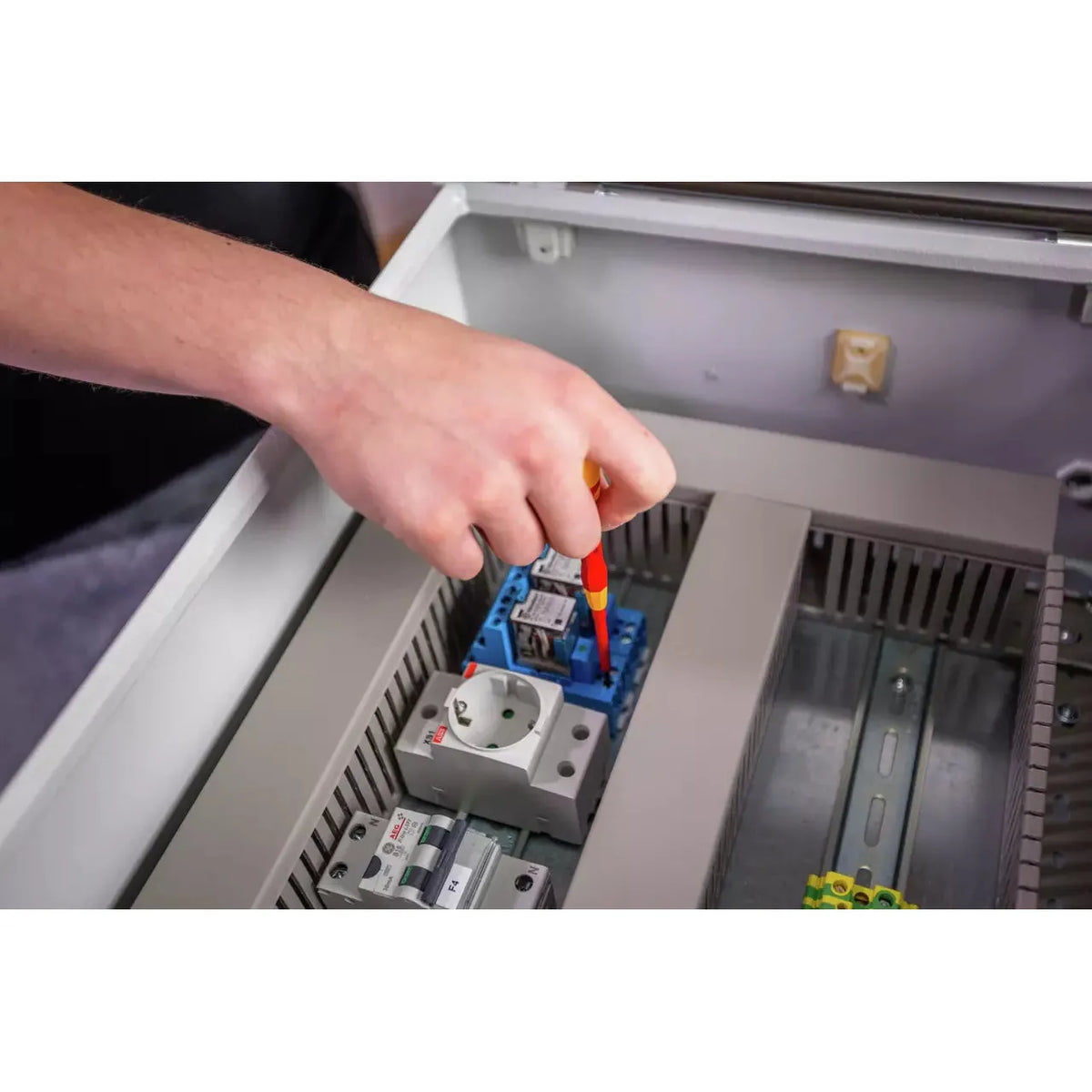 A person uses a fine screwdriver on an electrical component inside a control panel.