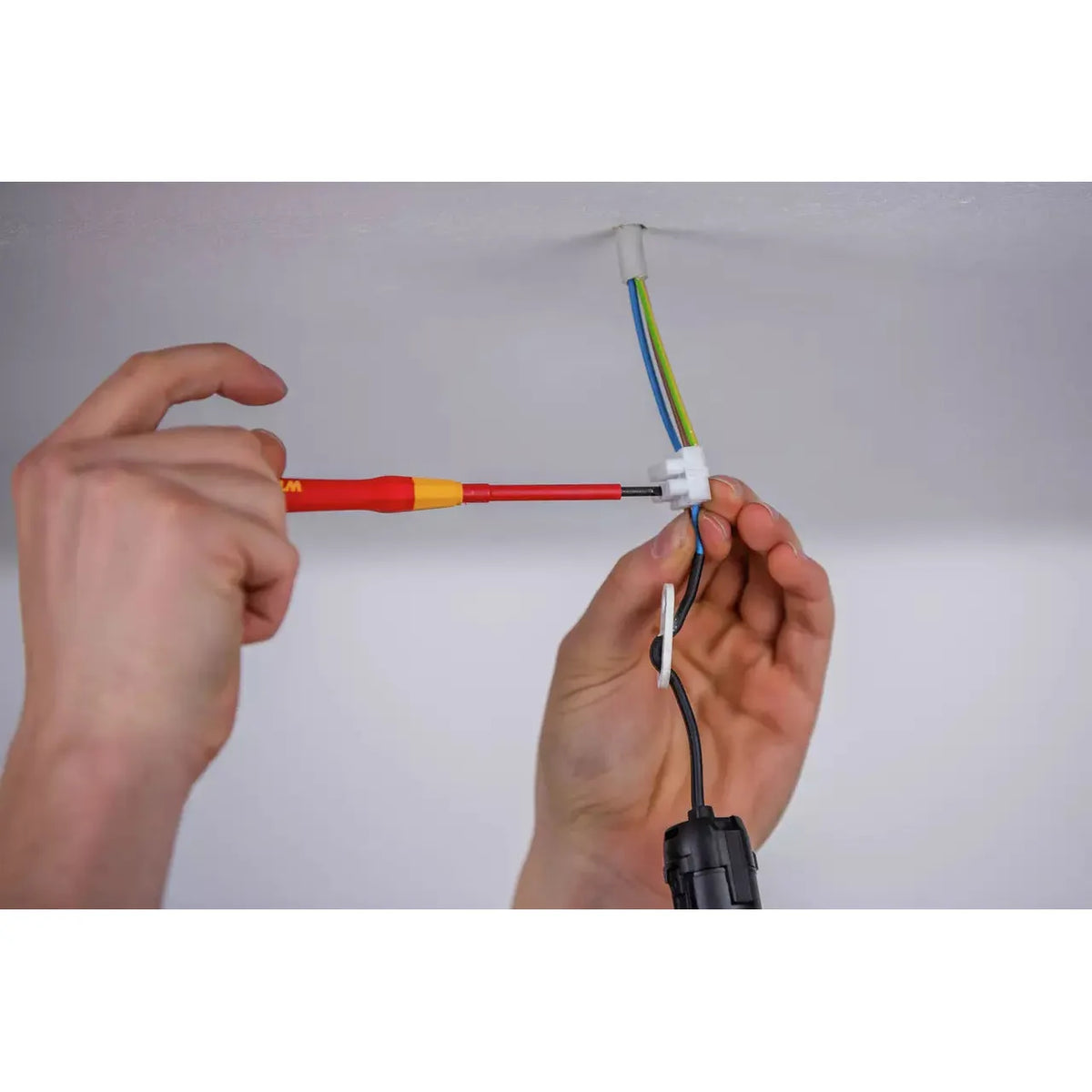 Person using a red and yellow fine screwdriver on electrical wiring in the ceiling.