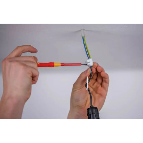 Person using a red and yellow fine screwdriver on electrical wiring in the ceiling.