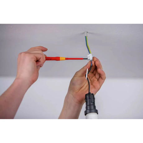Person using a red insulated screwdriver to work on ceiling electrical wires.