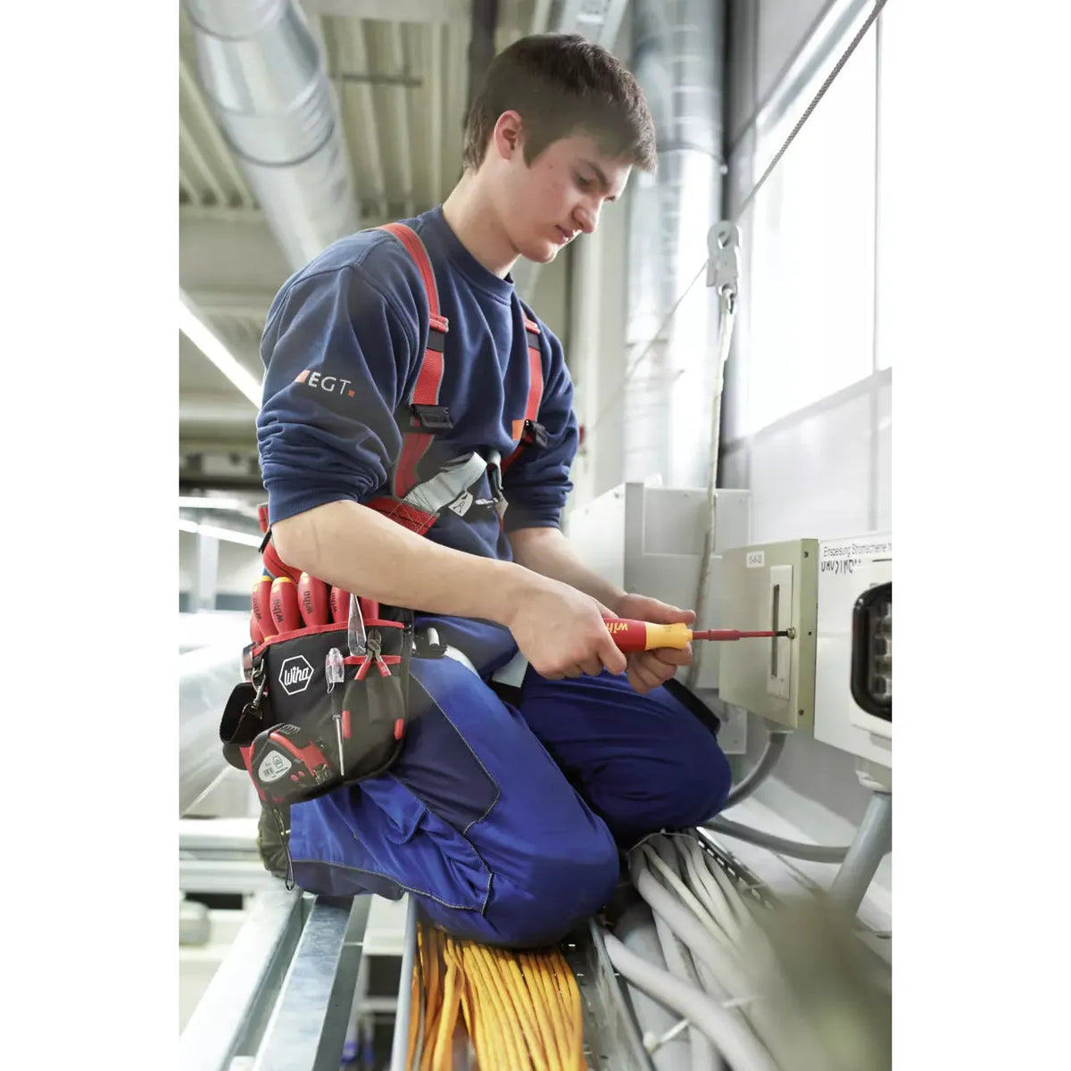 A person is working with an electric screwdriver on a control cabinet.