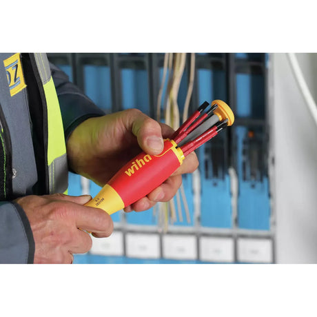 A person holding a red and yellow electric screwdriver with multiple bits in front of a circuit panel.
