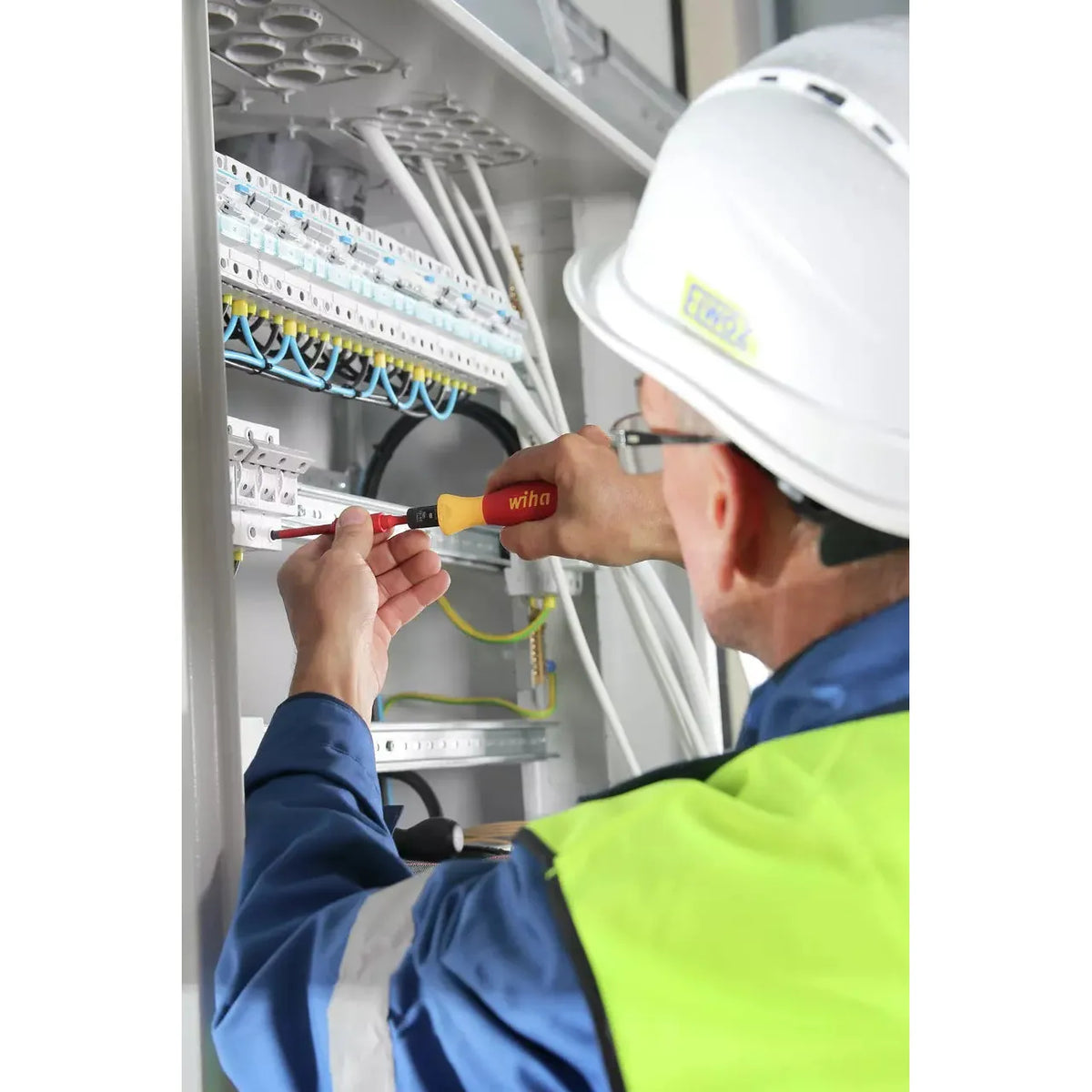 5-piece – A person uses an electric screwdriver on an electrical panel, wearing a hard hat and safety vest.