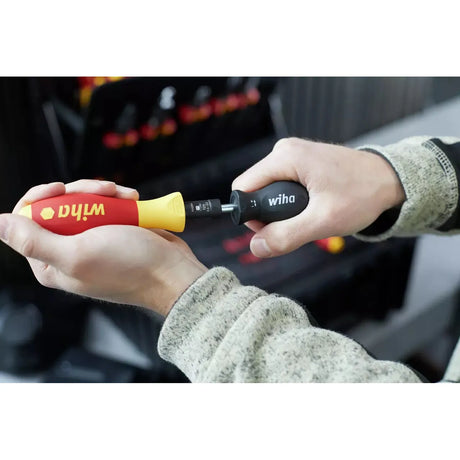 5-piece – Two hands holding a red and yellow screwdriver and a black tool in a workshop setting.