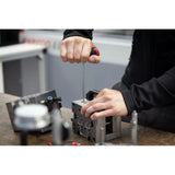 Person using a screwdriver to work on a metal block on a workbench.