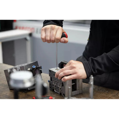 Person using a screwdriver to work on a metal block on a workbench.