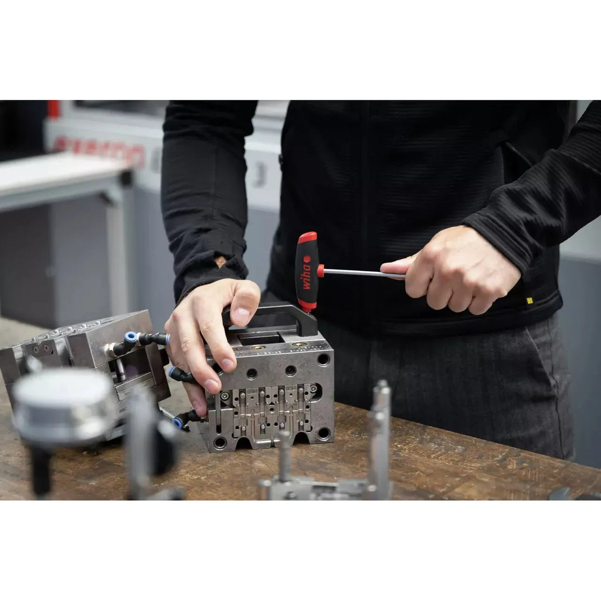 A person uses a T-handle wrench on a metal component at a workbench.