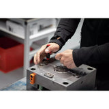 A person using a red-handled screwdriver on a metal mechanical part.