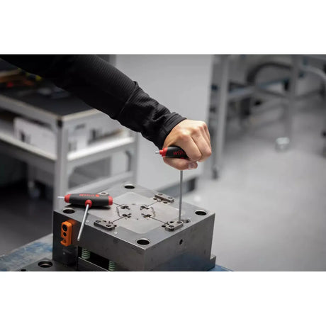 A person uses a hex key with a red and black handle on a metal fixture.