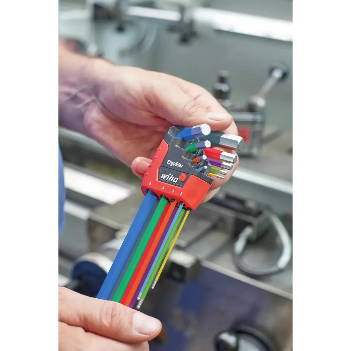 A person holds a set of colorful L-shaped hex keys in a red holder labeled "ErgoStar" in a workshop.