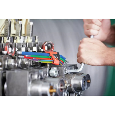 A person uses an L-wrench on industrial machinery with a colorful hex key set nearby.