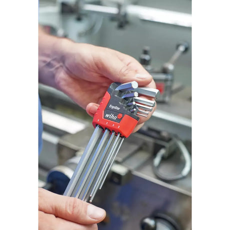 A person holds an ErgoStar hex key set with a red holder in a workshop.
