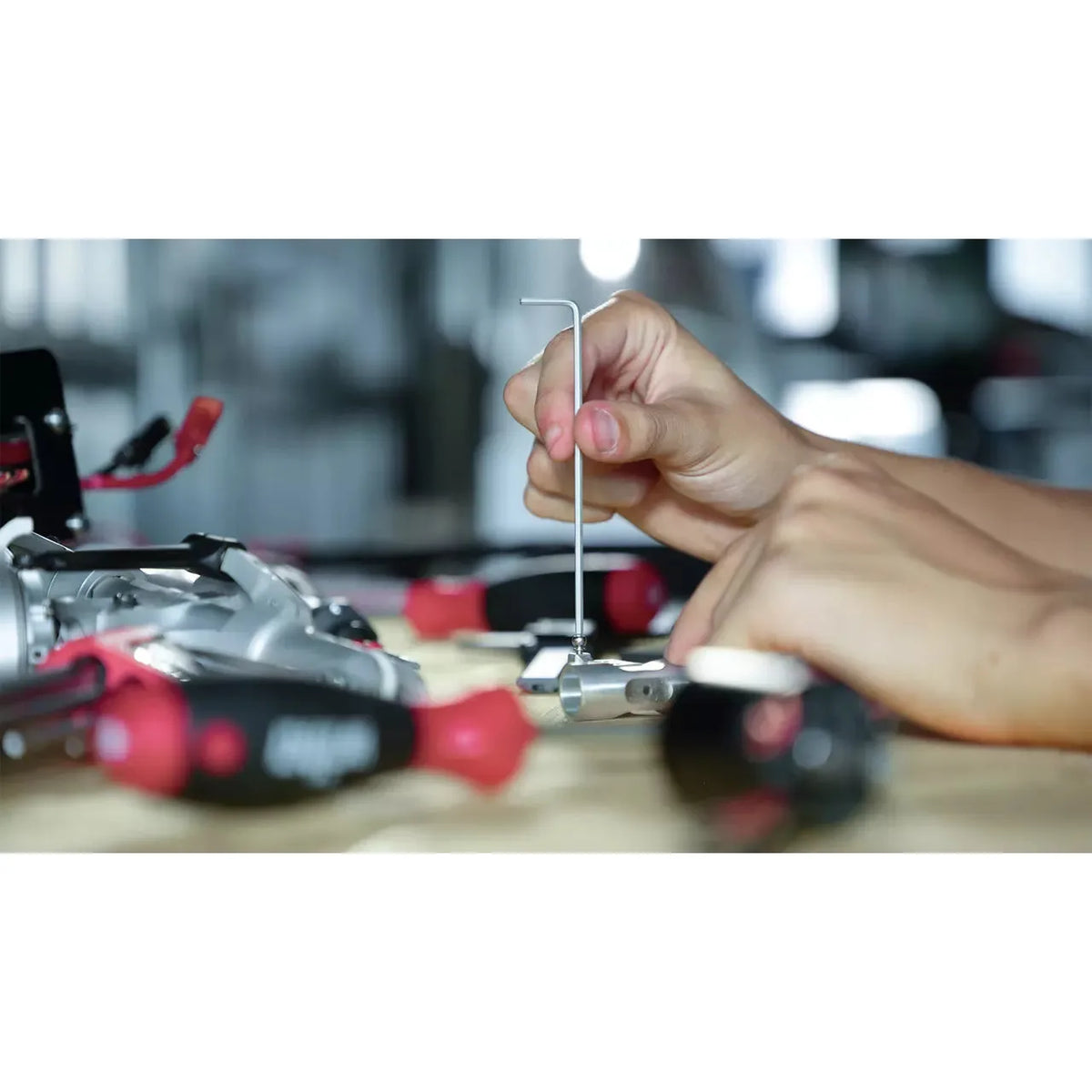 A person uses an L-shaped hex key on a small metal object, surrounded by tools.