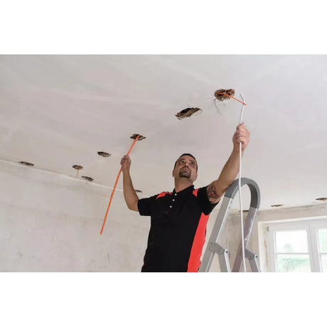 A person works on a ceiling, holding a measuring tape and a cable