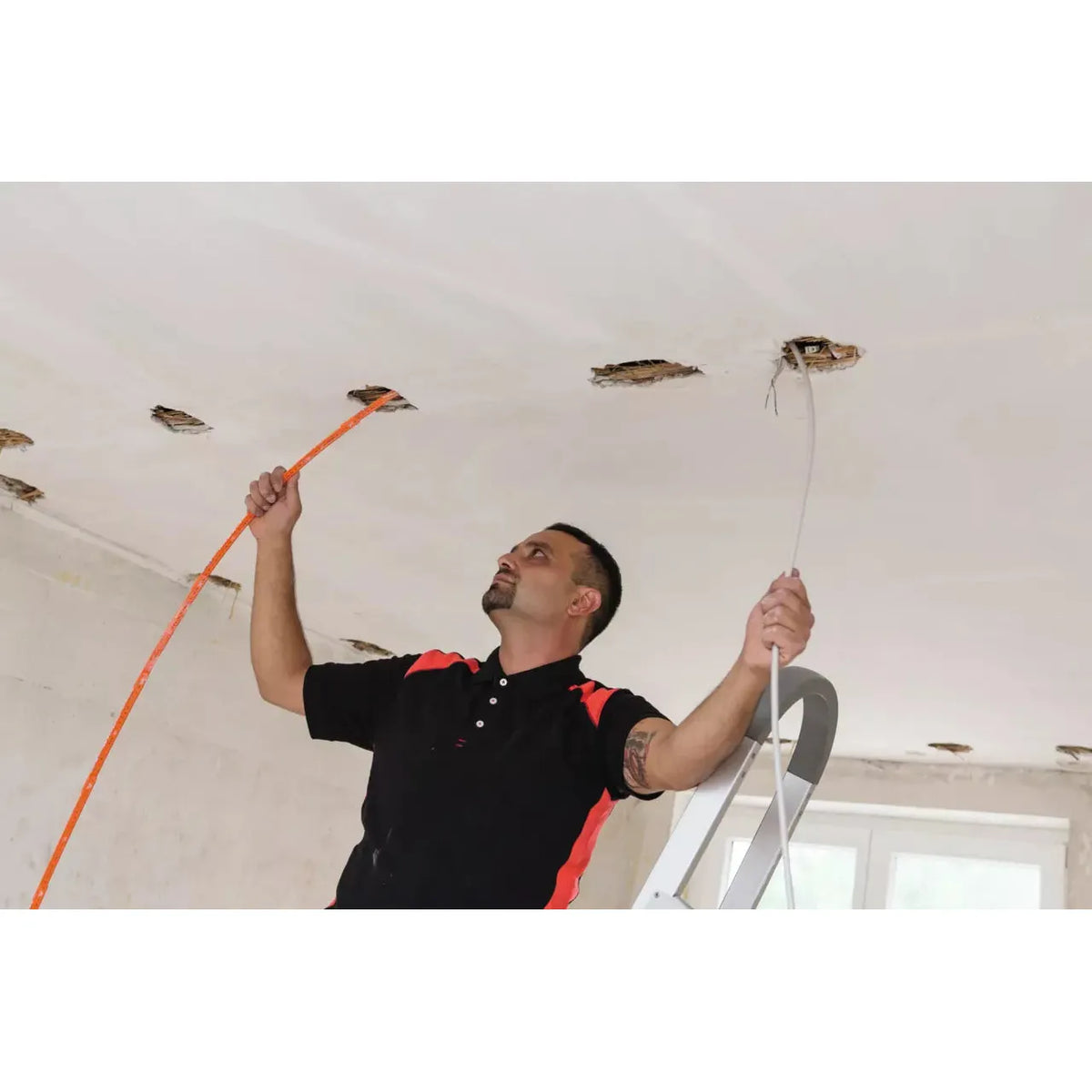 A man working on the ceiling with a folding ruler and cable