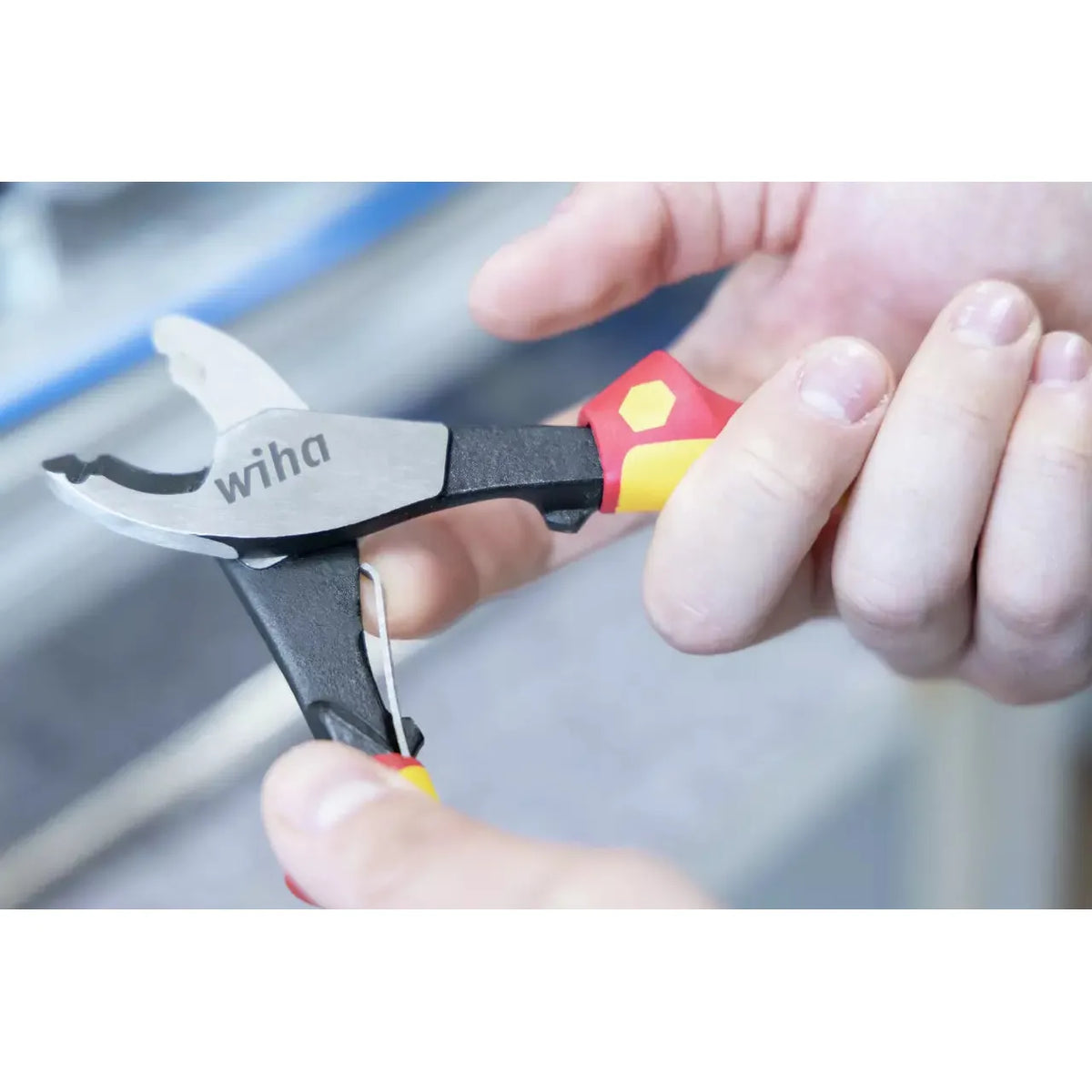 Person holding an industrial electric cable cutter with red and yellow handles